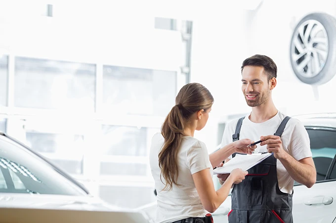 Kfz-Mechaniker im Gespräch mit Kollegin während Auftragsübergabe